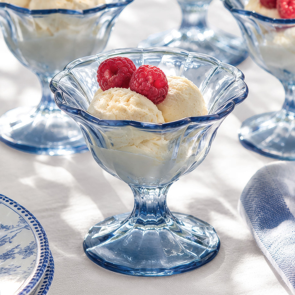 Blue footed glass dessert bowl filled with vanilla ice cream and raspberries on a blue and white table