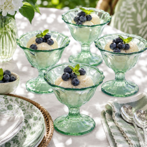 Four green glass dessert bowls filled with ice cream and blueberries on a garden table