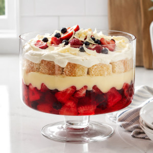 Clear glass pedestal trifle bowl filled with layered berry trifle on a white kitchen bench