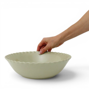 Hand holding the rim of the Maeve soft green serving bowl, showing its size against a white background