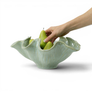 Hand arranging green pears in the Selena sea green display bowl against a white background