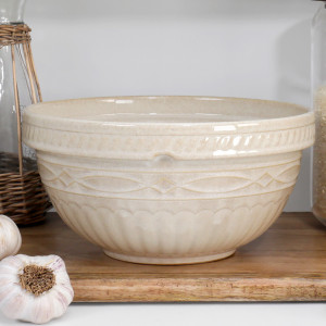 Beige ceramic mixing bowl with embossed geometric detailing styled on a wooden kitchen shelf beside pantry jars