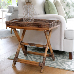 Brown rattan tray table styled with a glass vase beside an armchair