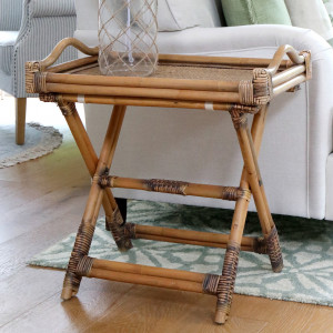 Brown rattan butler's tray table with folding cross-frame base beside a cream sofa