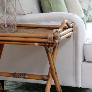 Side view of the brown rattan tray table showing its curved handle and folding cane frame