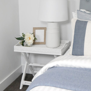 White rattan tray table styled as a bedside table with a lamp