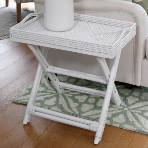 White woven tray table viewed from the side beside a sofa
