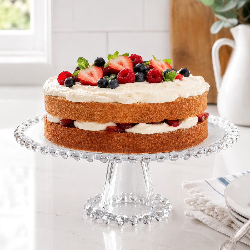 Clear beaded glass cake stand holding a layered sponge cake topped with fresh berries