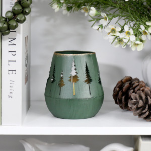 Green forest tealight holder glowing on a white shelf beside pine cones, books and white flowers