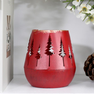 Close-up of unlit red metal tealight holder with tree cut-outs, a rounded base and distressed gold-coloured rim