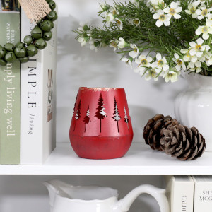 Red metal forest tealight holder displayed unlit on a white shelf beside pine cones, books and white flowers