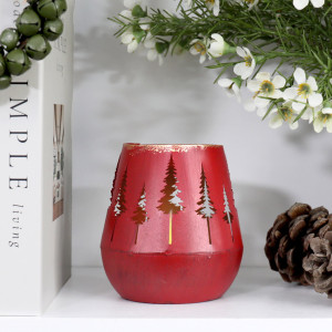 Red forest tealight holder with light glowing through tree cut-outs, styled beside books and pine cones