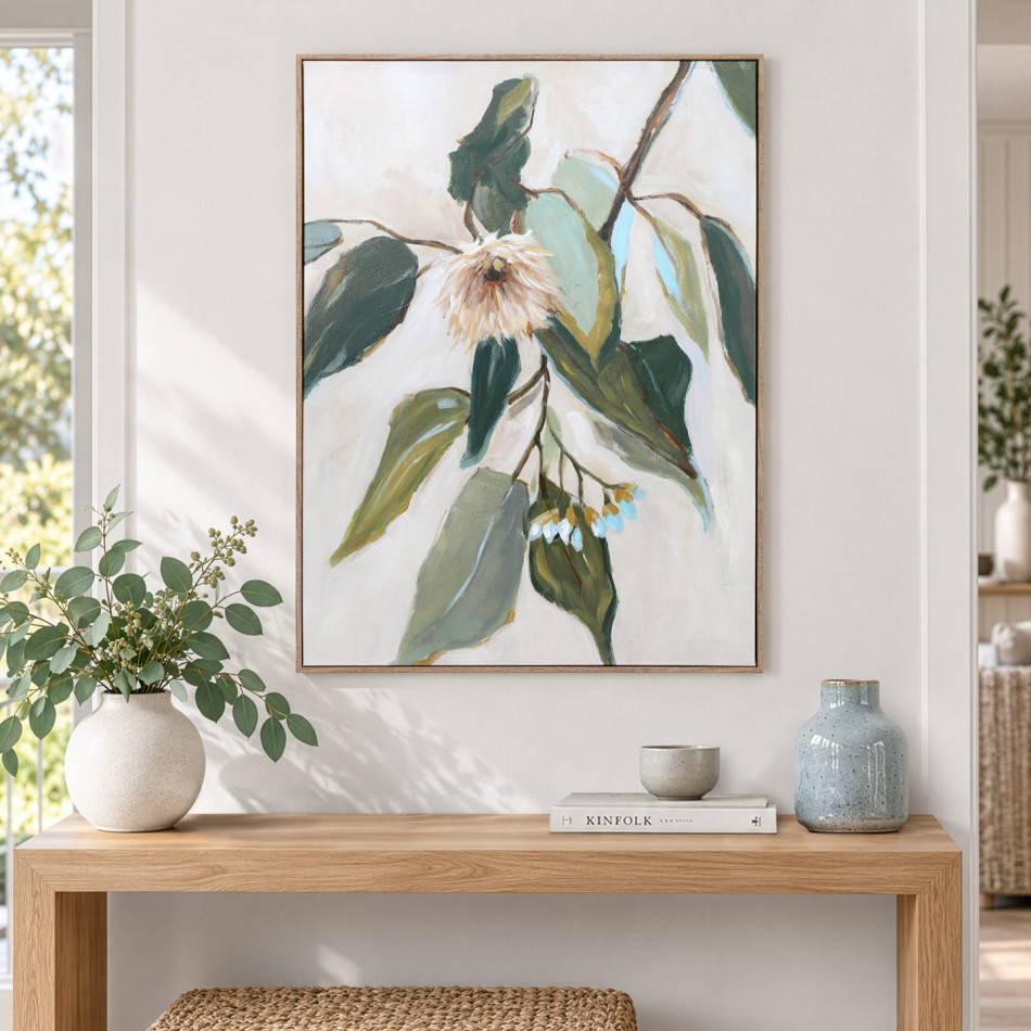 Framed eucalyptus artwork above a timber console styled with leafy stems, ceramic vases and stacked books