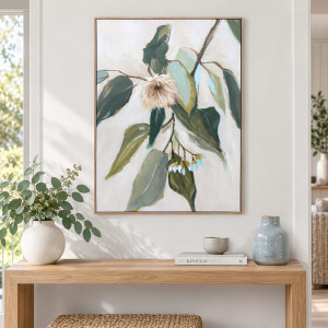 Framed eucalyptus artwork above a timber console styled with leafy stems, ceramic vases and stacked books