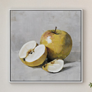 White-framed golden apple still life canvas hanging on a pale wall, showing a whole apple, half and wedge