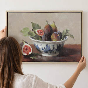 Person positioning framed fig still life canvas with a blue-and-white bowl against a white wall