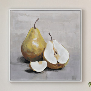 White-framed golden pear still life canvas hanging on a pale wall, showing whole and cut fruit