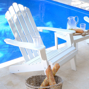 White folding Adirondack chair beside a pool with drinks and bread on a side table