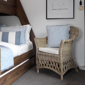 Antique-grey rattan armchair styled with a blue cushion beside a wood bed