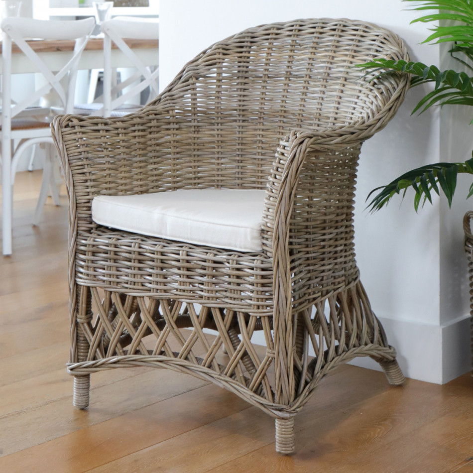 Charlotte woven rattan armchair with cream cushion beside a plant in a bright dining area