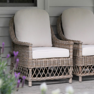 Pair of antique grey rattan armchairs with cream cushions on a covered verandah