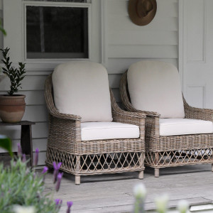 Pair of rattan armchairs with cream cushions and purple flowers in the foreground