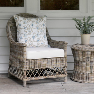 Antique grey rattan armchair with floral cushion beside a woven side table
