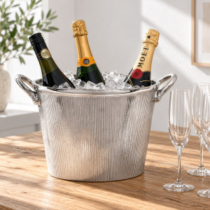 Silver champagne bucket with ice and three bottles beside champagne flutes on a wooden table