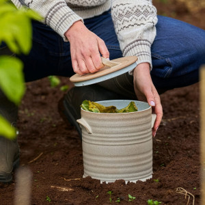 Lidded Brantham ceramic compost bin held beside a garden compost area