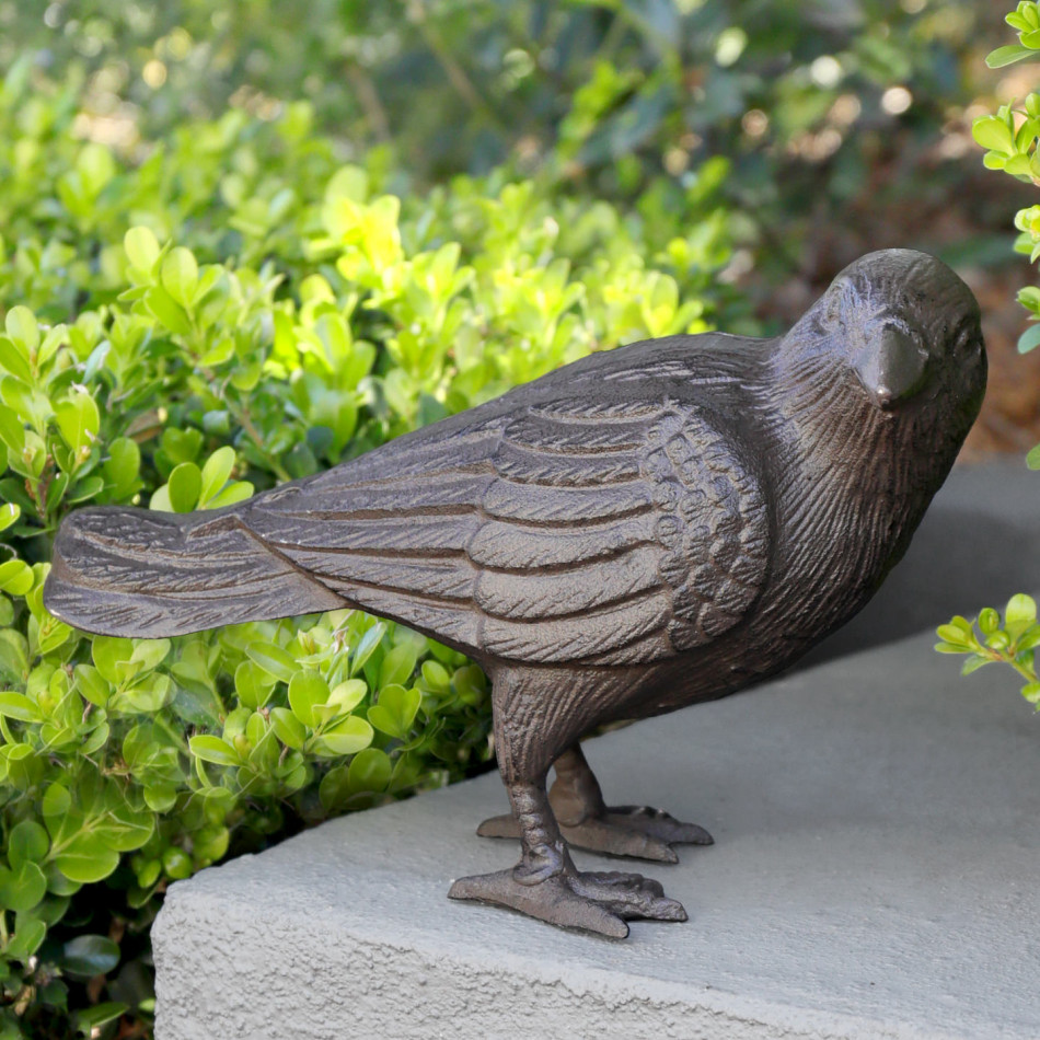 Close-up of dark brown cast iron crow with layered feather detail on a grey garden wall