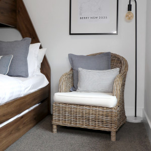 Devon rattan armchair styled beside a bed with a grey decorative cushion