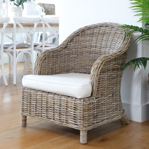 Antique grey-brown rattan armchair with cream cushions beside a white dining setting
