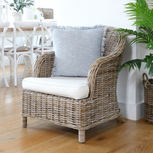 Front angled view of rattan armchair with cream cushions and a blue-grey accent cushion