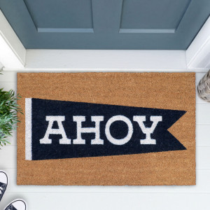 Close-up of a coir doormat with a navy AHOY pennant beside a blue-grey front door
