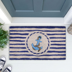 Nautical anchor doormat on white floorboards beside greenery and navy sneakers at a blue-grey door
