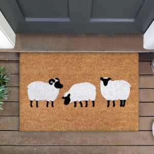 Sheep-patterned coir doormat below a dark door, with surrounding timber boards and greenery visible