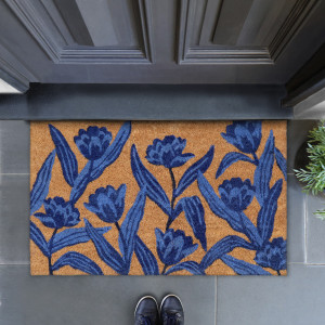 Miranda blue tulip doormat below a panelled grey door, with navy shoes and greenery nearby