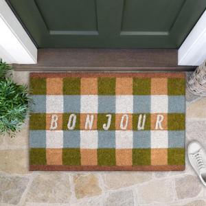 Bonjour gingham doormat at a green front door, with leafy greenery, a woven basket and a white sneaker