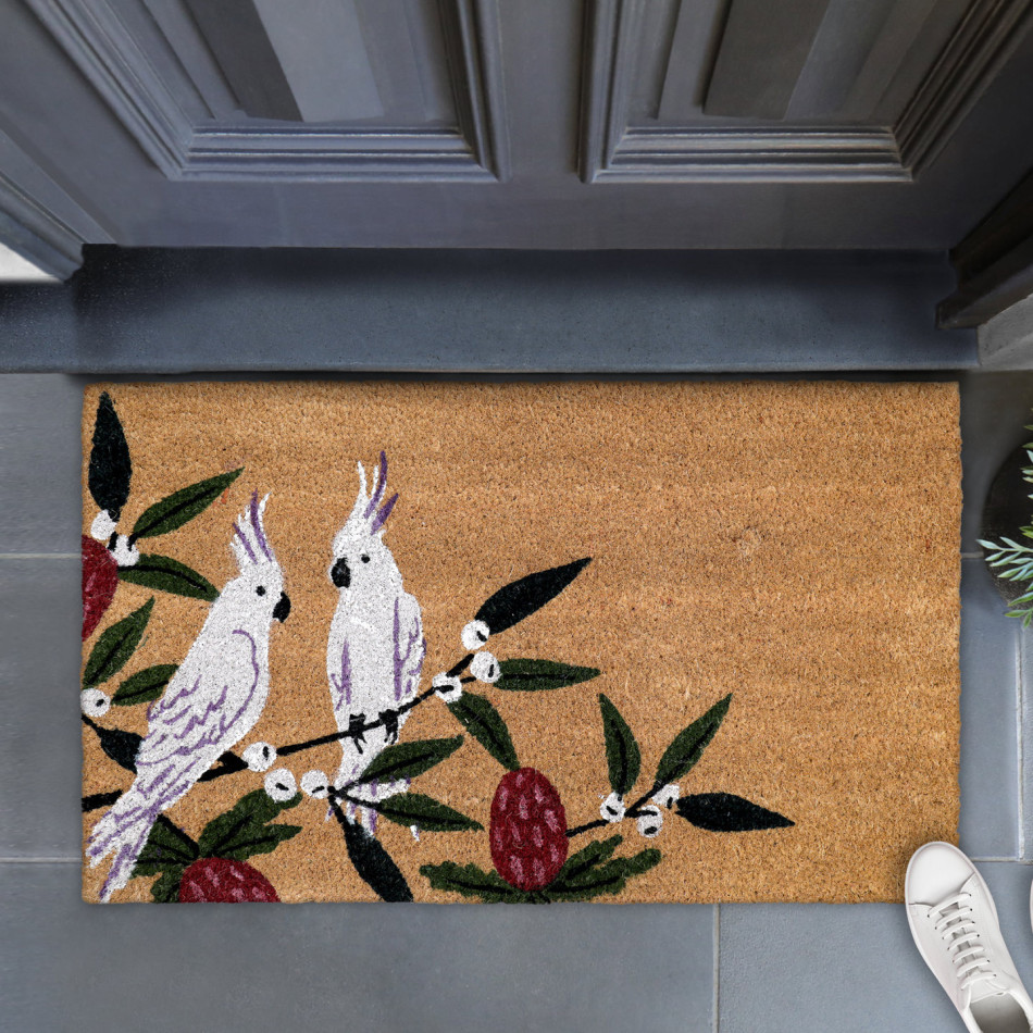Close-up of a coir doormat with two white cockatoos, green leaves and burgundy blossoms beside a dark door