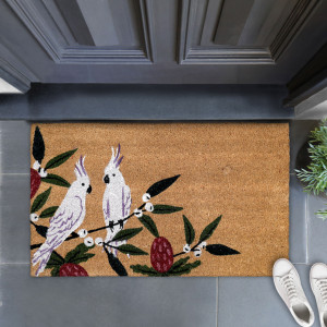 Cockatoo coir doormat at a dark front door, styled with greenery and white shoes on grey tiles