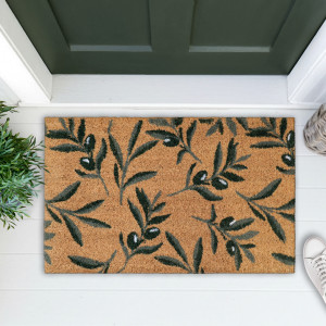 Olive leaf coir doormat on white floorboards beside greenery and a white sneaker at a green door