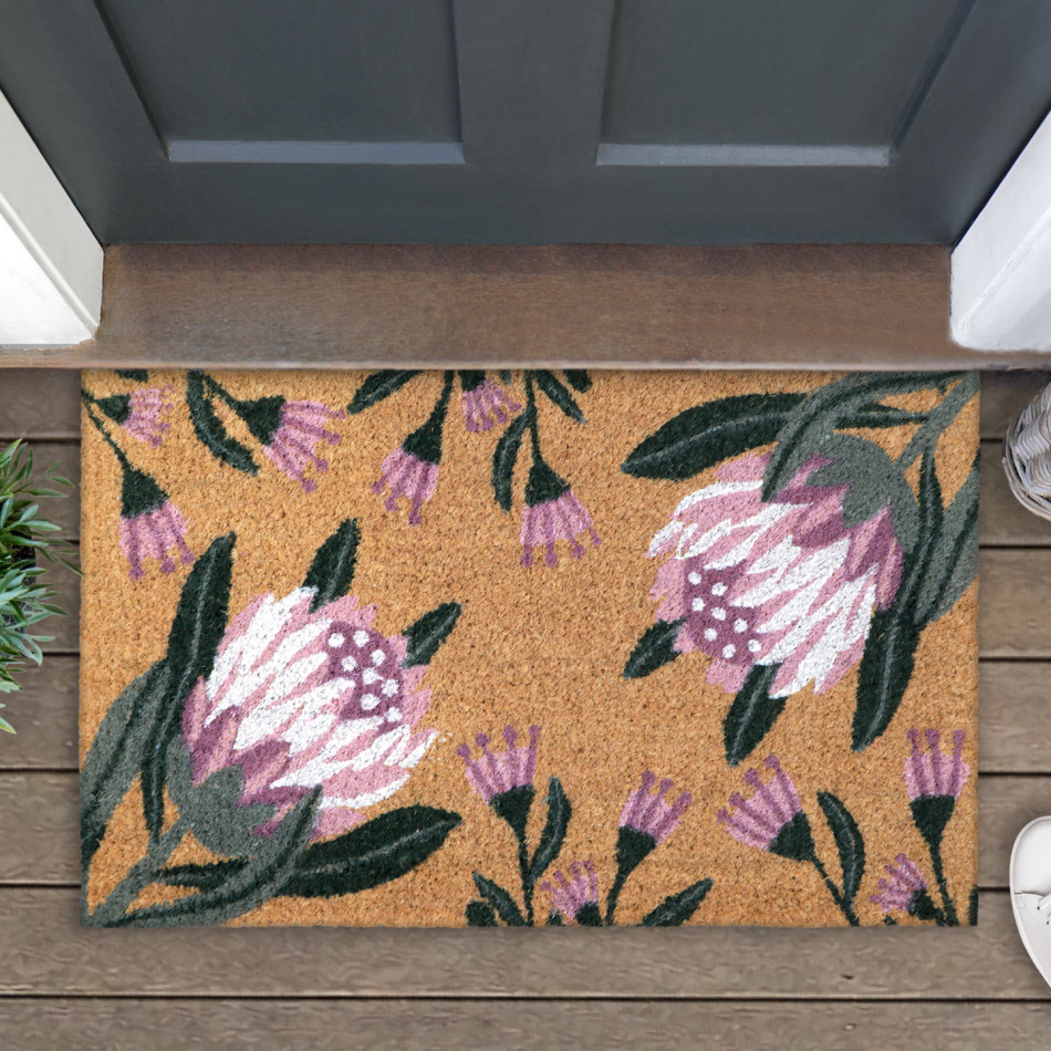 Close-up of a natural coir doormat with pink proteas and green leaves beside a dark front door