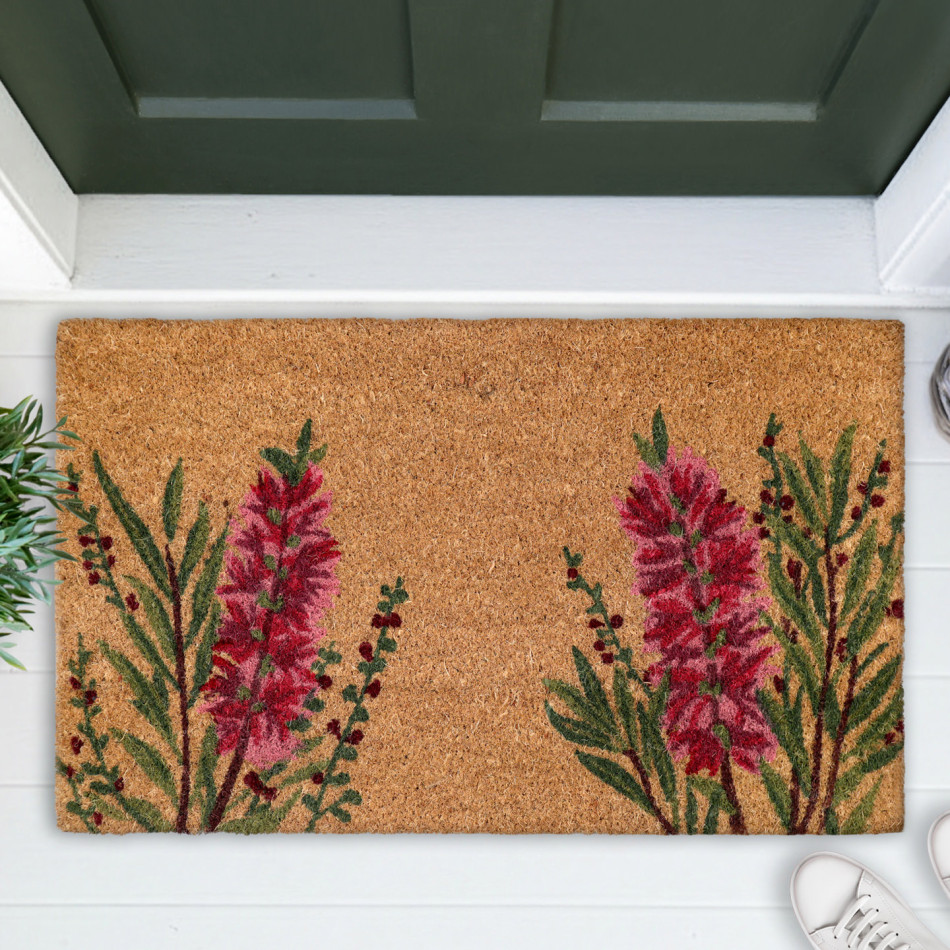Red bottlebrush coir door mat shown close up on white boards beneath a green door