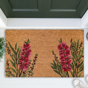 Red bottlebrush coir door mat shown close up on white boards beneath a green door