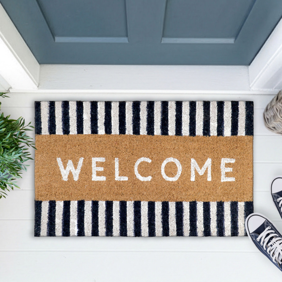 Navy-and-white striped welcome doormat at a blue-grey door with greenery, a woven basket and navy shoes