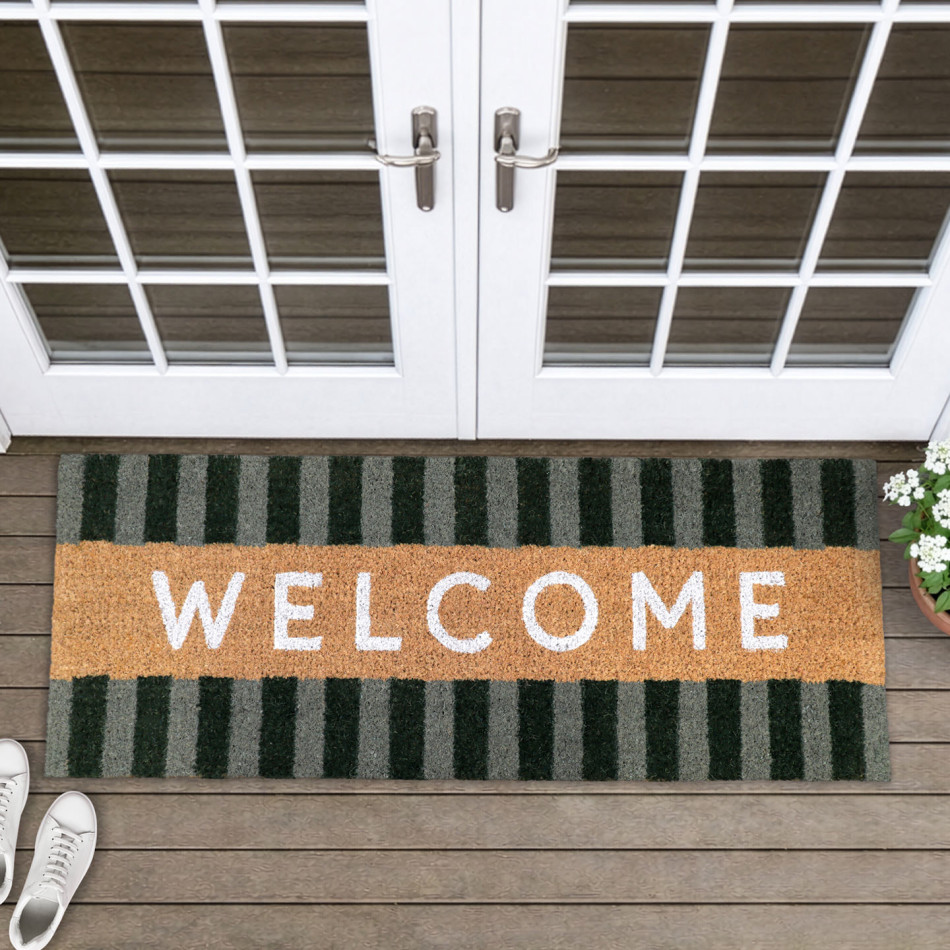 Long coir welcome doormat with green striped borders at white French doors, beside white flowers and shoes