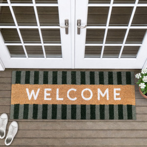 Green striped welcome doormat on timber boards beneath white French doors, with white shoes and potted flowers