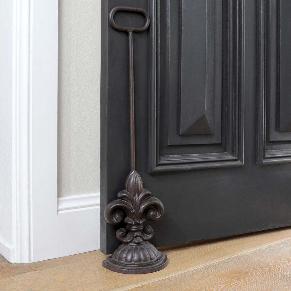 Dark brown cast iron fleur-de-lis door wedge with tall handle holding open a black door