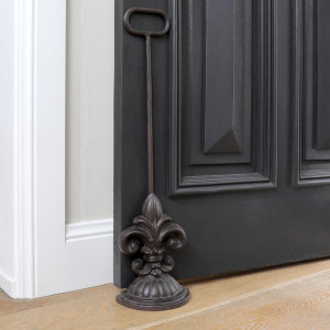 Dark brown cast iron fleur-de-lis door wedge with tall handle holding open a black door