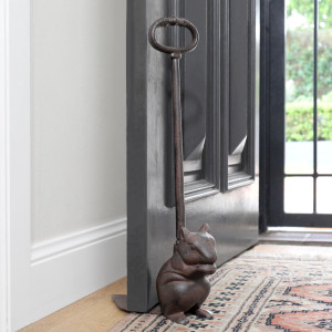 Tall dark brown cast iron squirrel door wedge holding open a black door beside a patterned rug